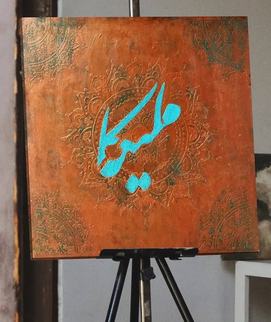 خوش‌نویسی نام ملیکا با رنگ فیروزه‌ای روی تابلو پتینه‌ی نارنجی